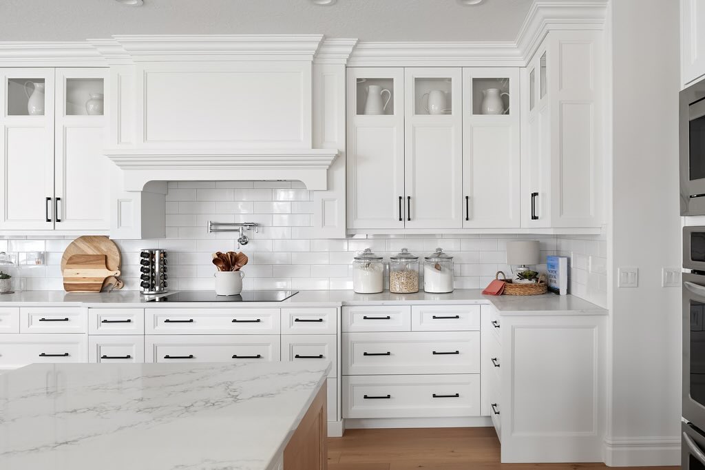 A modern white kitchen with sleek marble countertops and matching white cabinets