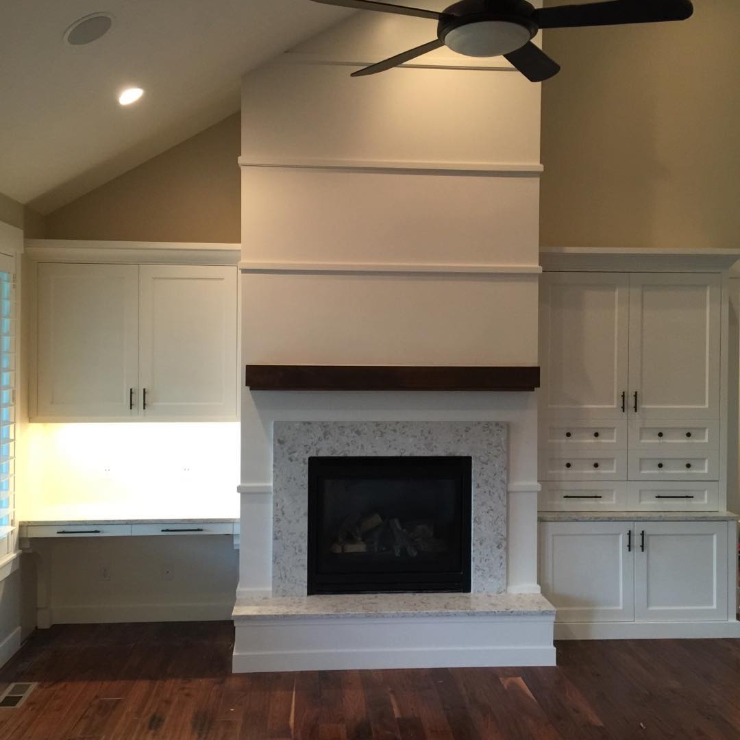 A cozy fireplace in a room with white cabinets and a ceiling fan